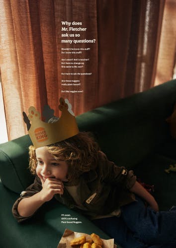 Image of a print ad for Burger King's A Little More Confusing campaign, showing a child sat on a green sofa wearing a Burger King paper crown with a pile of plant based Nuggets on the sofa, headlined 'Why does Mr Fletcher ask us so many questions?'