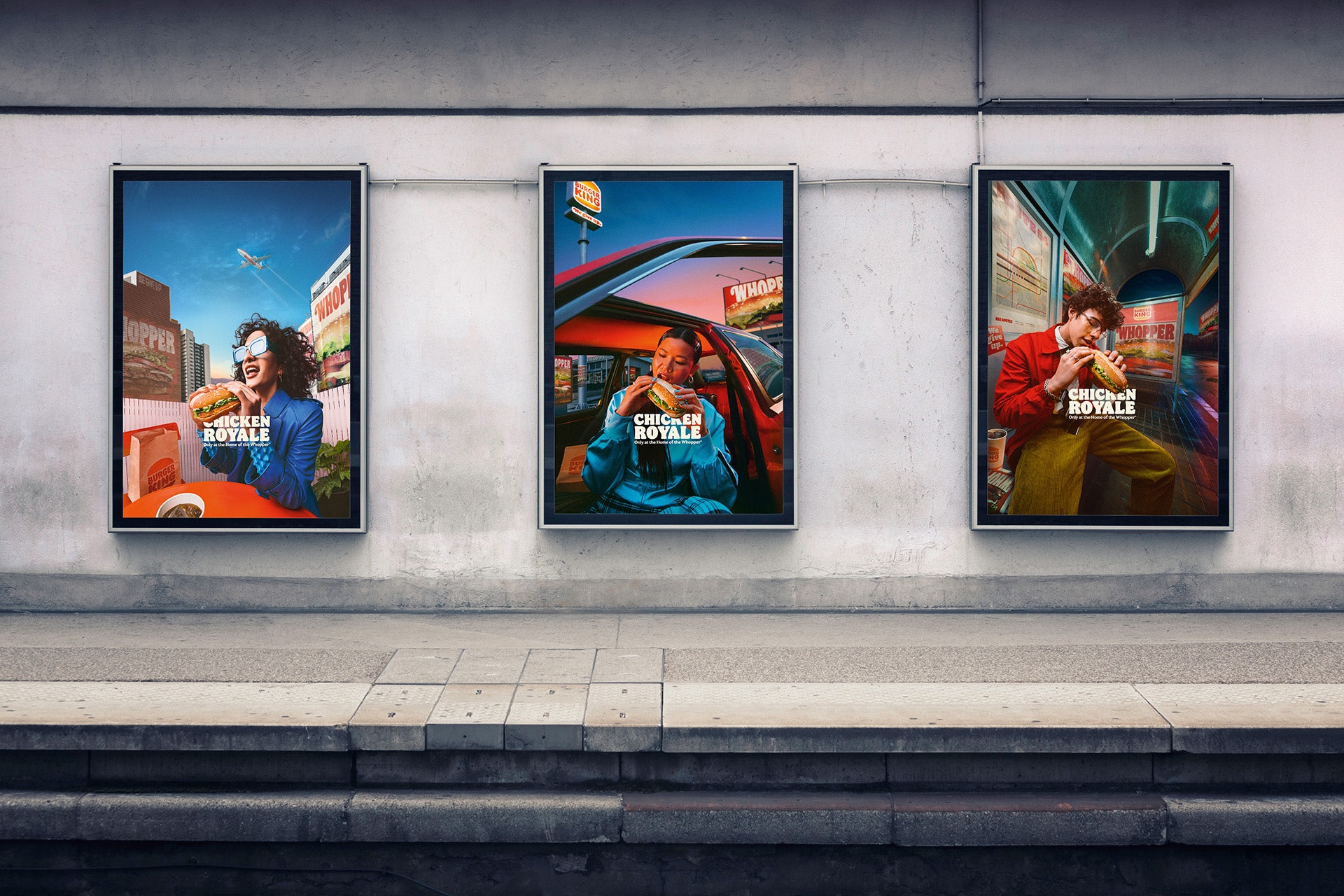 Photo of three vertical outdoor posters for Burger King, each showing a person wearing a colourful outfit eating a Chicken Royale, displayed inside a station