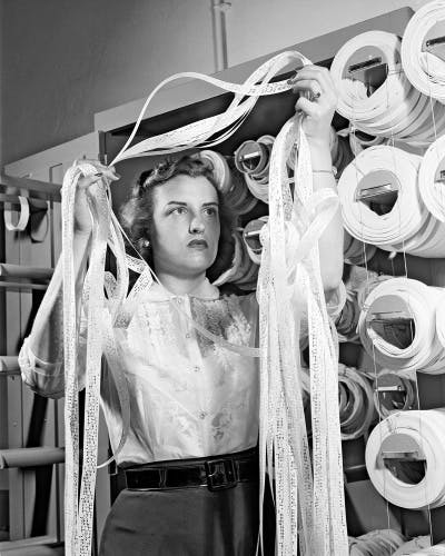 Black and white photograph showing a person in a white shirt with curly, coiffed hair, holding a pile of tape above their head