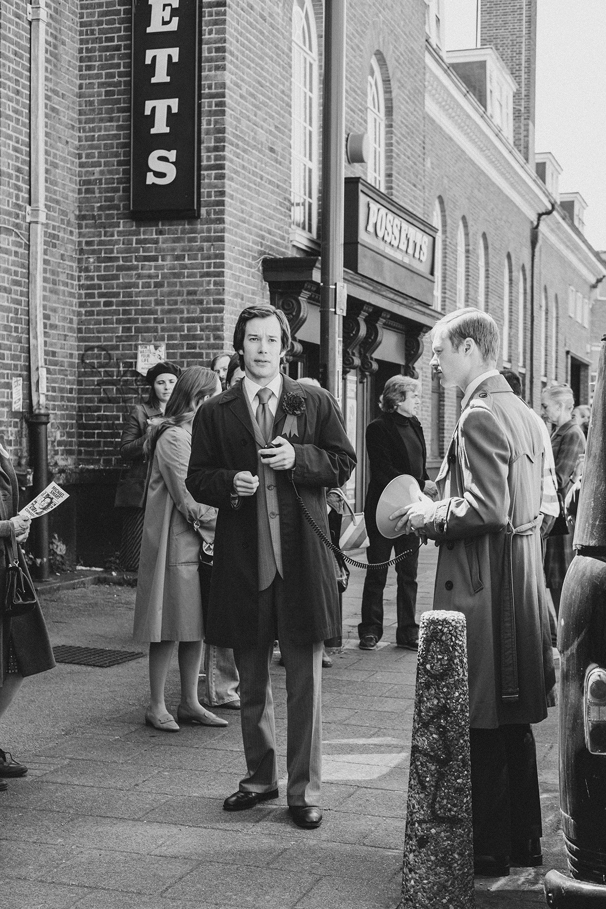 Black and white photograph by David Hurn for Black Mirror, showing a crowd of people dressed in the style of the 1970s gathered outside a shop named Possetts