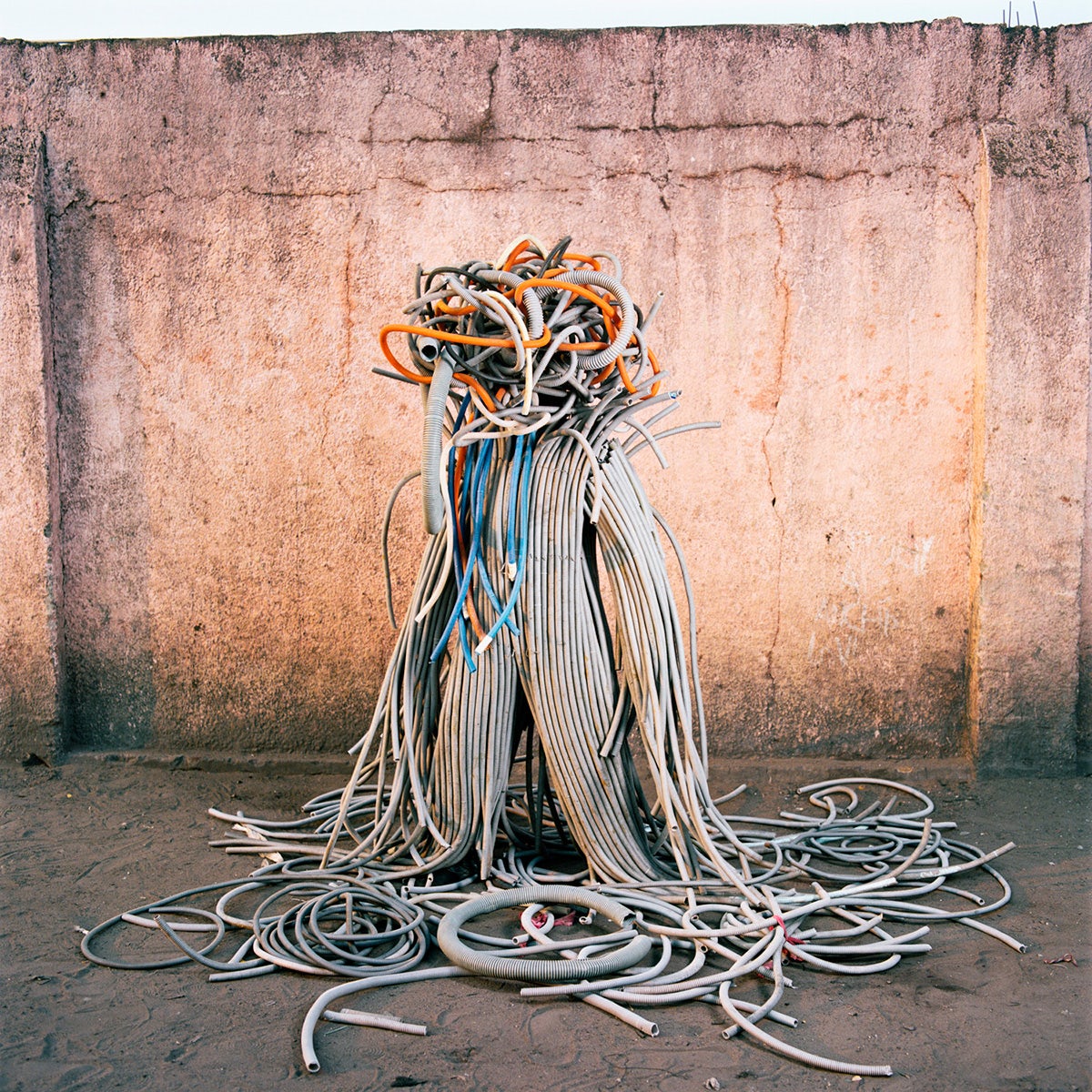 Photo by Colin Delfosse showing a person wearing a costume made out of old tubes, with the appearance of having tentacles, stood in front of a peach coloured wall