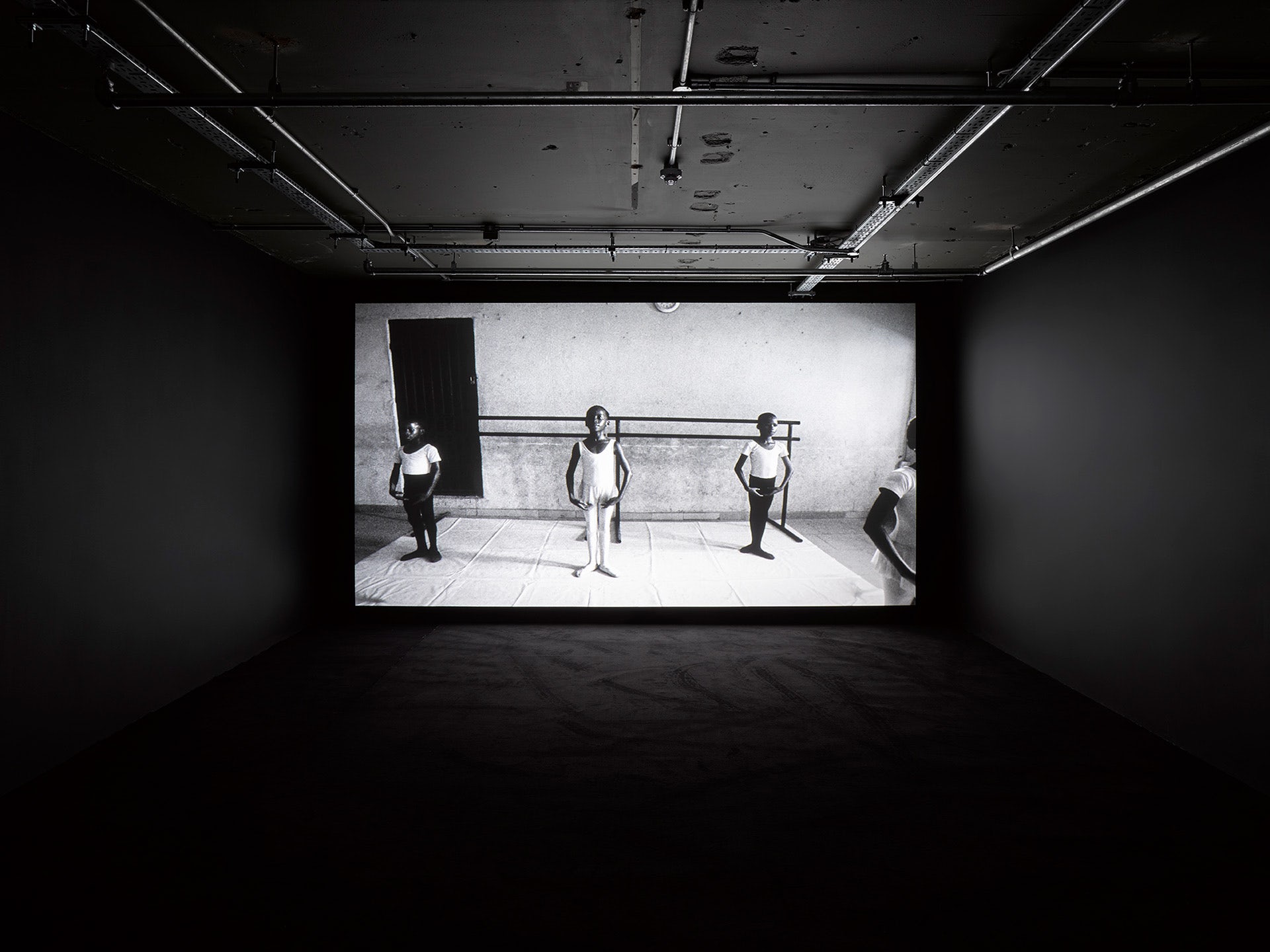 Photograph showing ballet dancers poised in Gabriel Moses's film Ijo, installed in a darkened room at 180 Studios