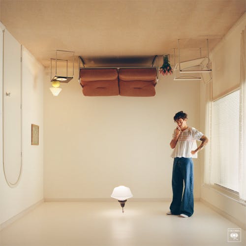 Image of the Harry's House album cover, showing Harry Styles stood looking at a lamp in a room where the sofa is on the ceiling