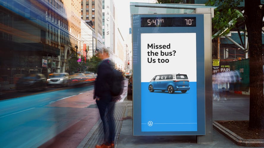 Photo of a vertical VW ID Buzz poster in a busy city street, with the tagline 'Missed the bus? Us too' above a two-tone blue and white VW bus against a matching blue and white background